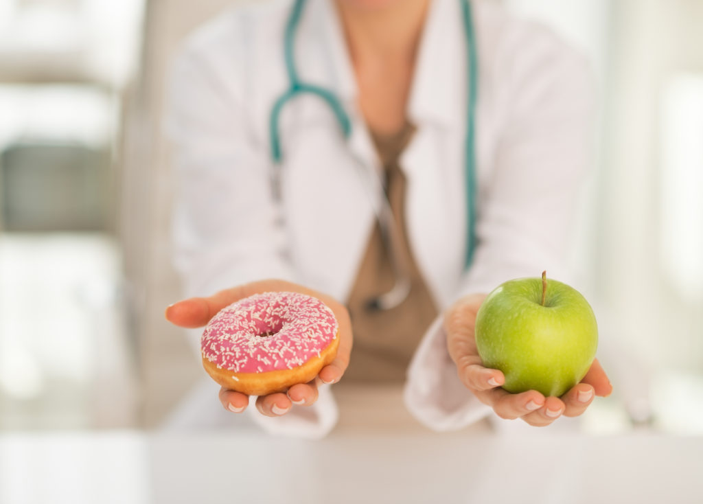 Closeup on medical doctor woman giving a choice between apple and donut